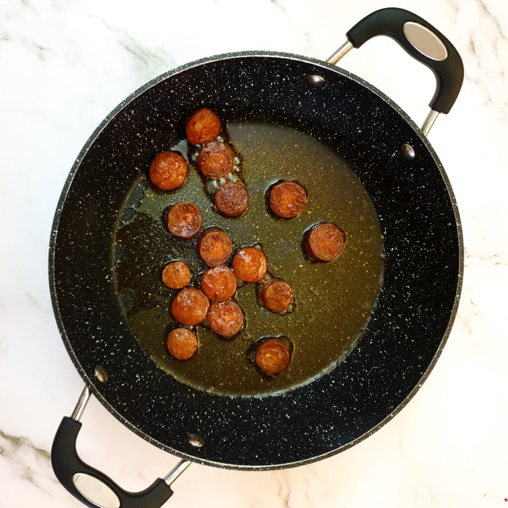 Slices of chorizo sausage being lightly fried in a pan.