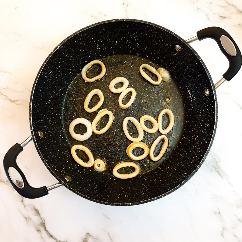 Calamari rings being lightly fried in a pan.