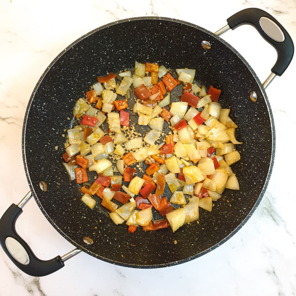 Tomatoes and red peppers being softened in a pan.