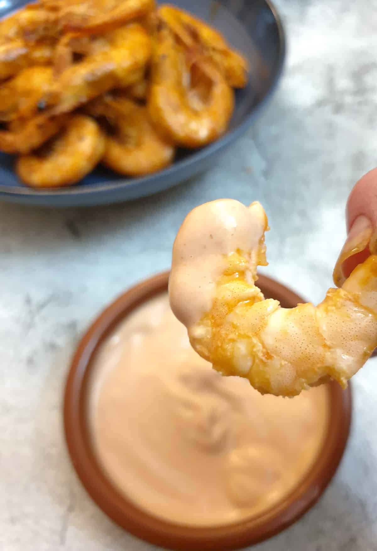 A peeled garlic butter prawn being dipped in marie rose sauce.