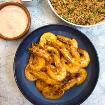 A dish of garlic butter prawns in their shells on a serving dish next to a bowl of fried rice and a pink dipping sauce.