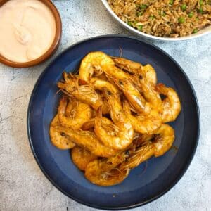 A dish of garlic butter prawns in their shells on a serving dish next to a bowl of fried rice and a pink dipping sauce.