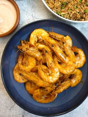 A dish of garlic butter prawns in their shells on a serving dish next to a bowl of fried rice and a pink dipping sauce.