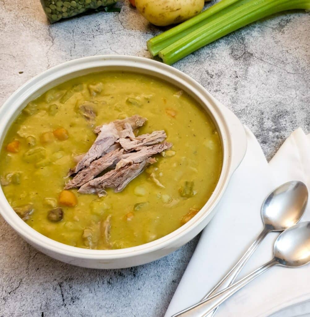 A serving dish of pea and ham soup garnished with extra shredded ham hock.