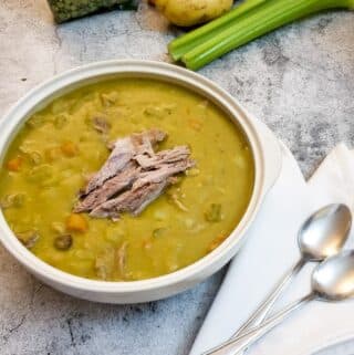 A serving dish of pea and ham soup garnished with extra shredded ham hock.