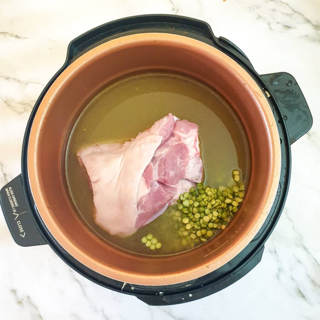A ham hock with split peas with stock in a pressure cooker.