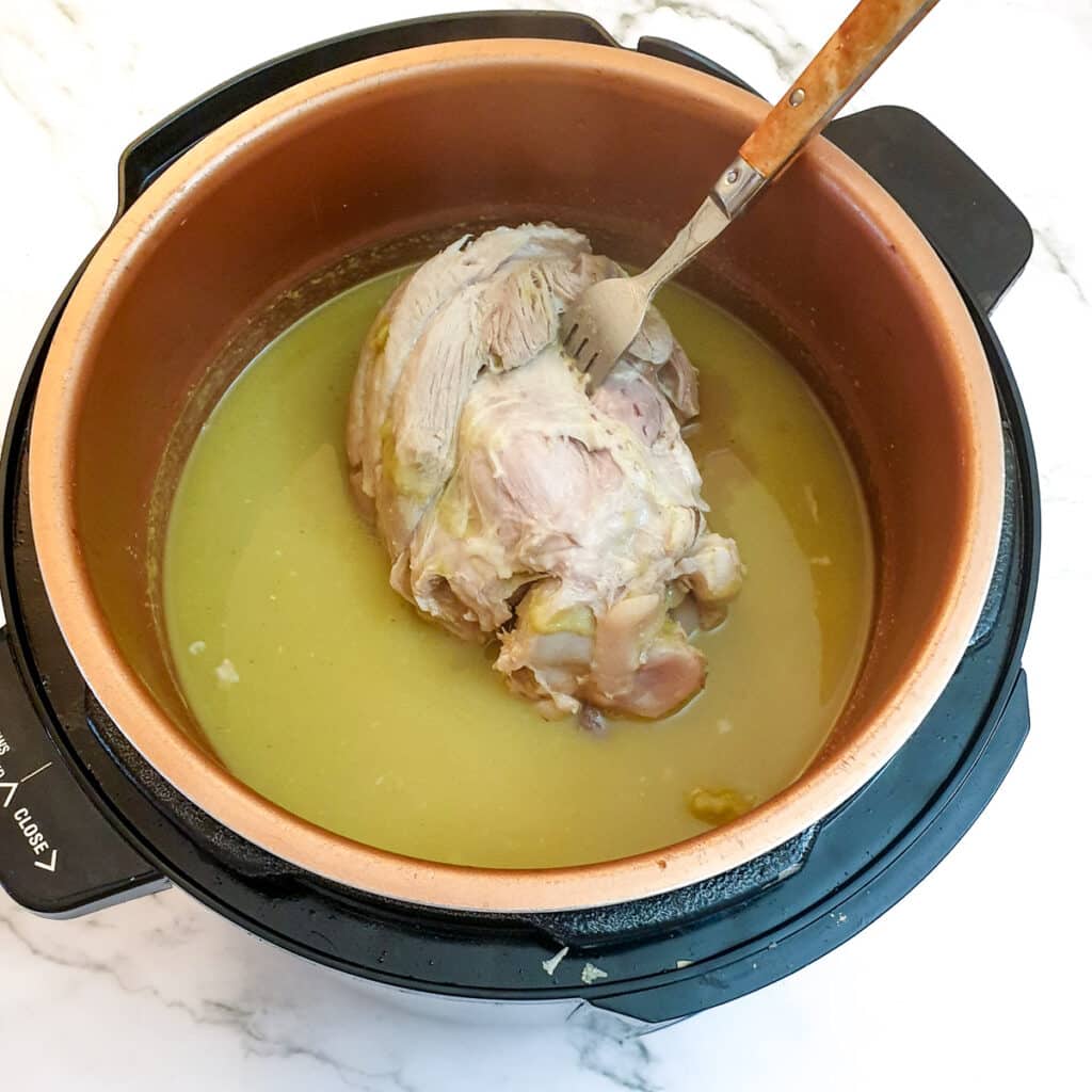 A cooked ham hock in a pressure cooker, being pierced with a fork.