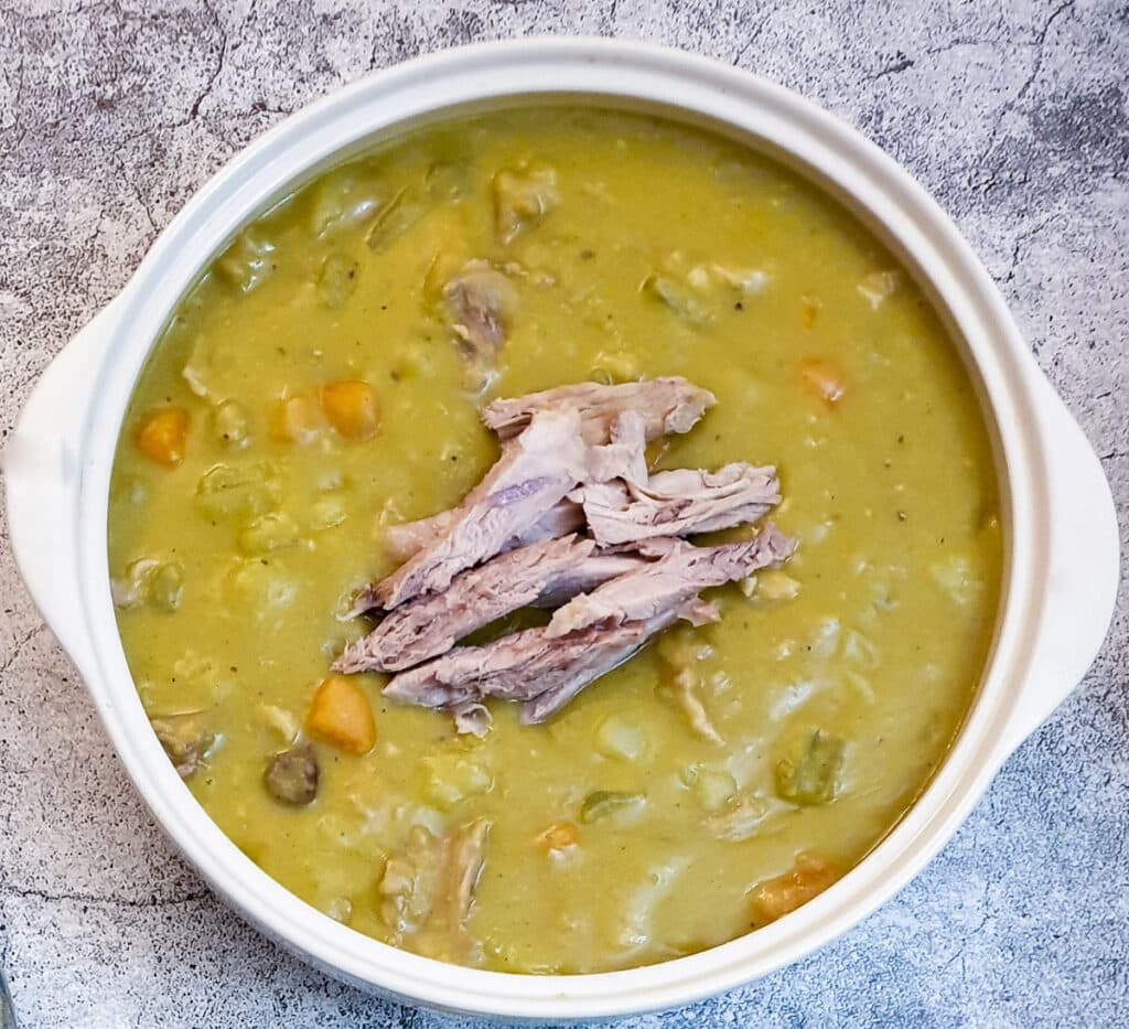 Split pea and ham soup in a serving bowl, garnished with shredded ham.