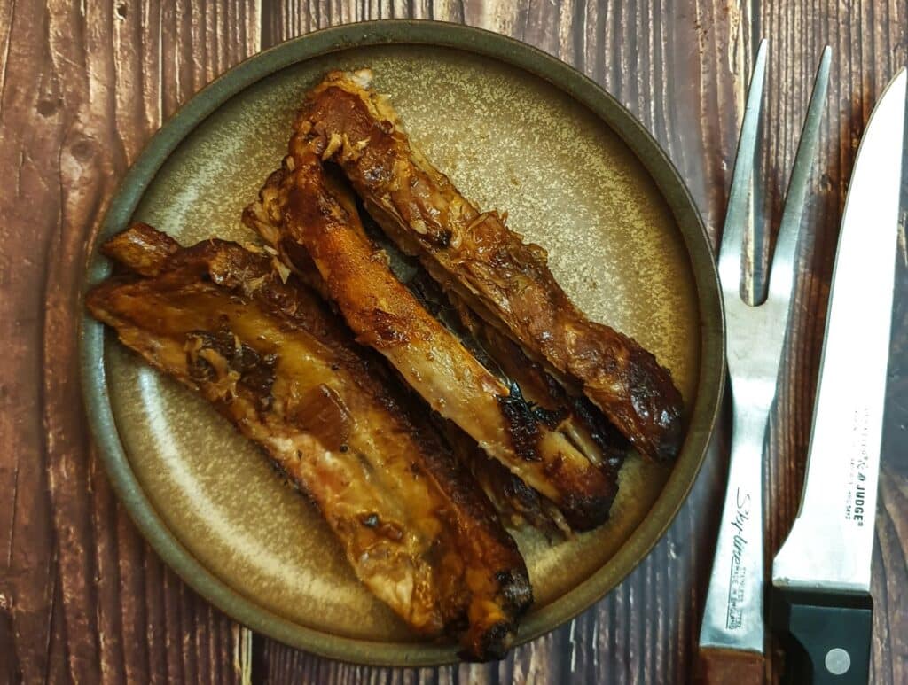 Three cooked barbeque pork spare ribs on a plate.