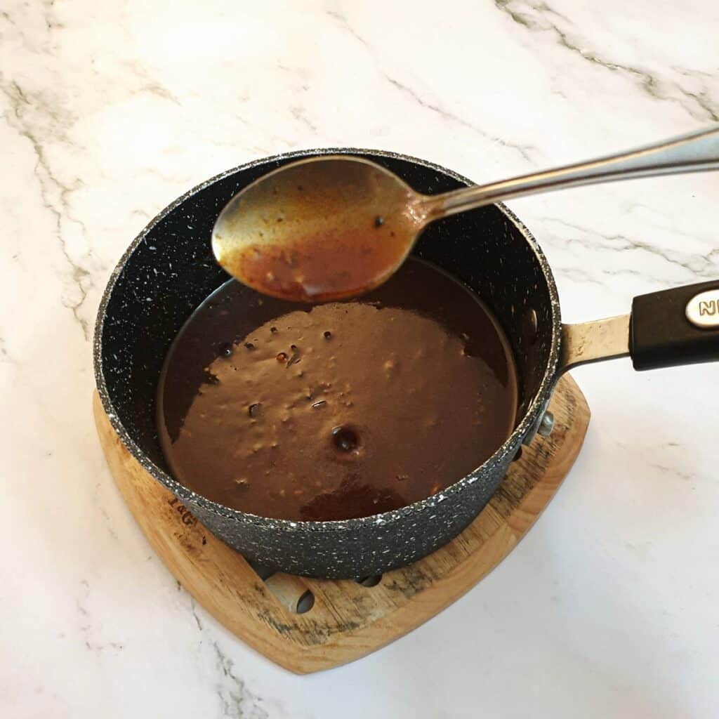 Barbeque sauce in a saucepan with a spoon showing the thickness of the sauce.