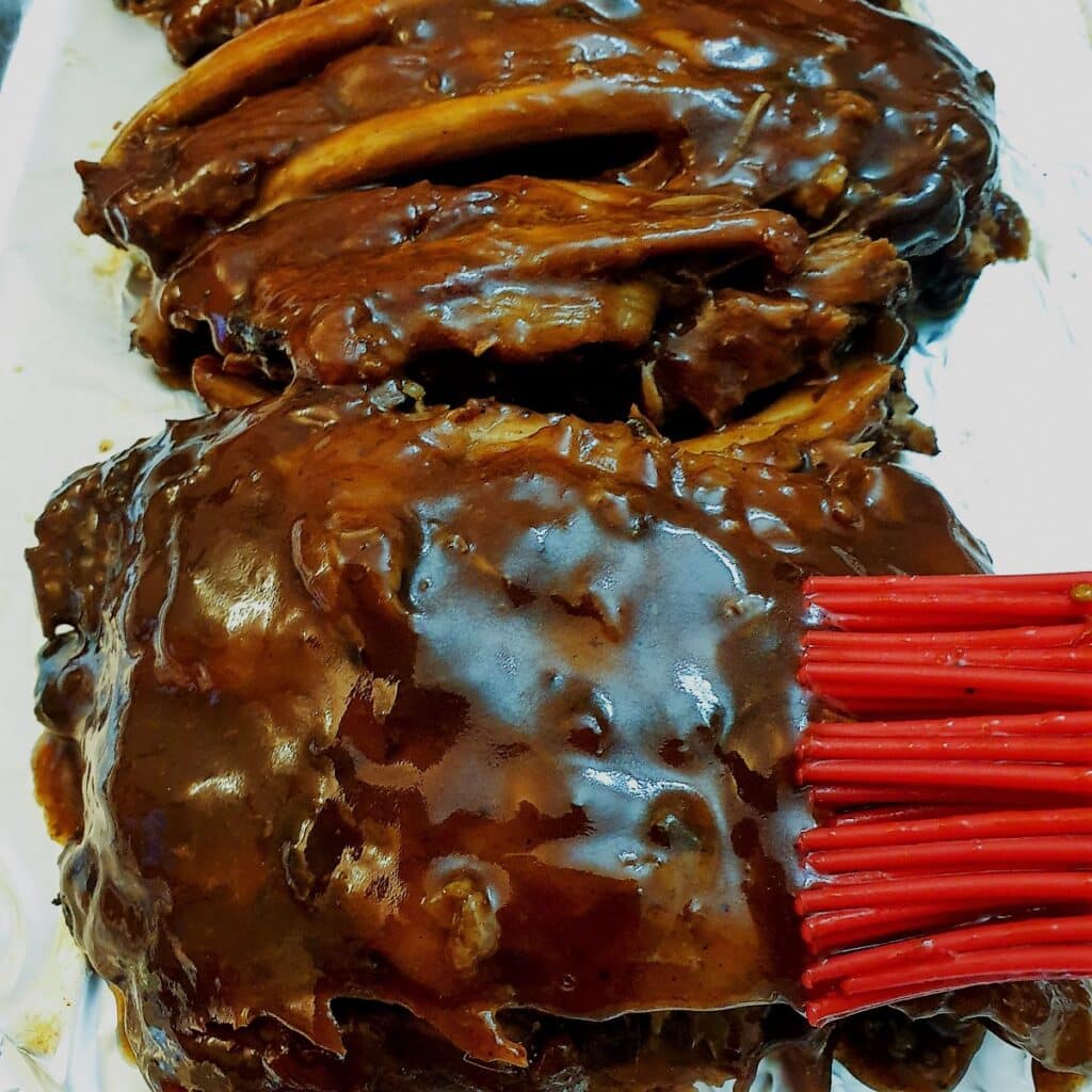 Barbeque sauce being brushed onto cooked spare ribs.