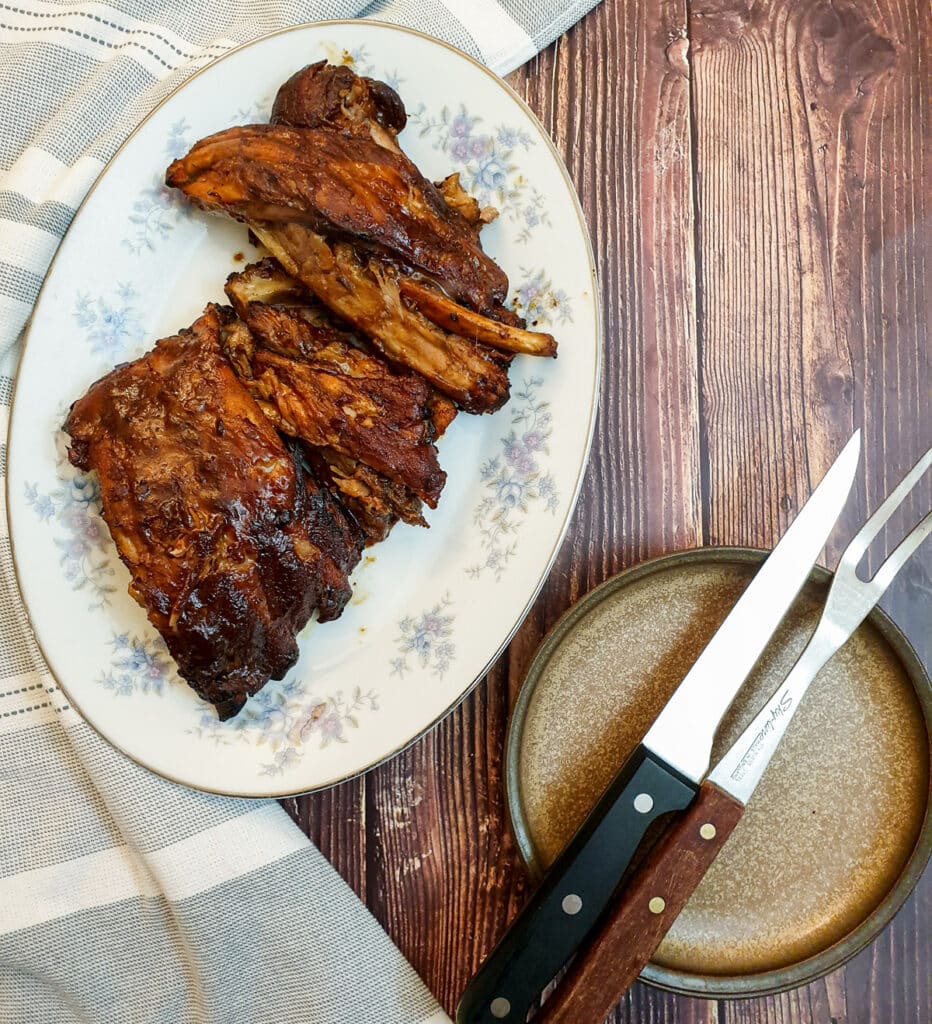 Barbeque spare ribs on a plate next to a knife and fork.