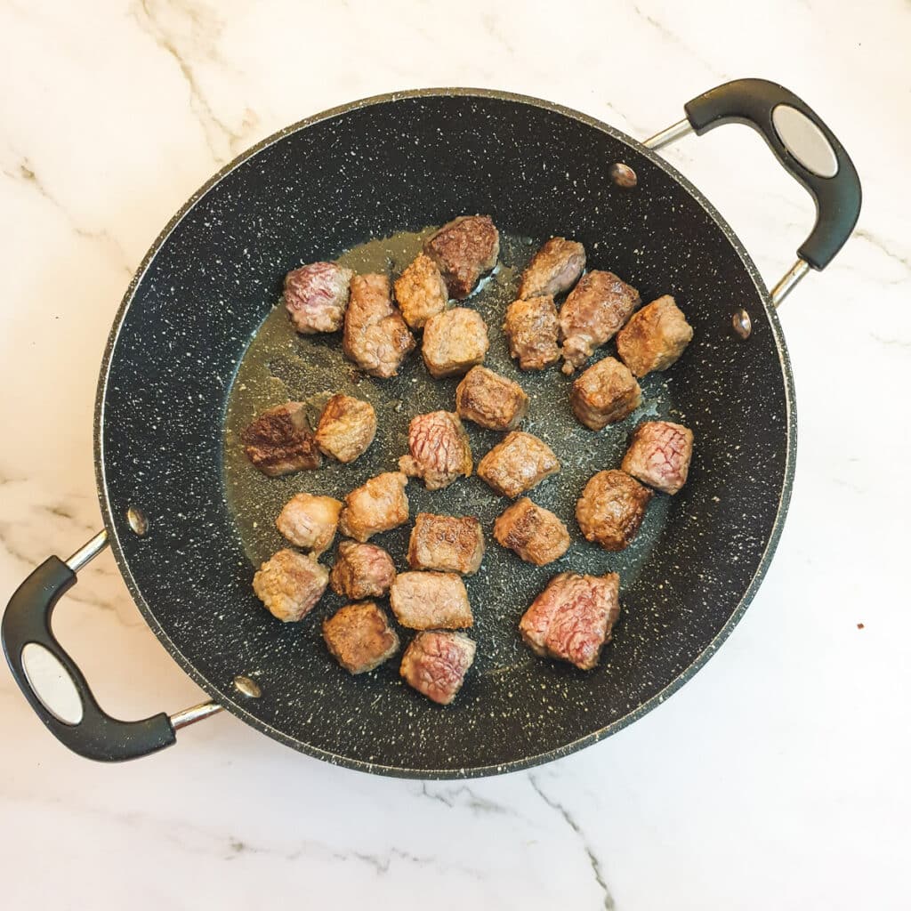 Steak pieces being browned in a frying pan.