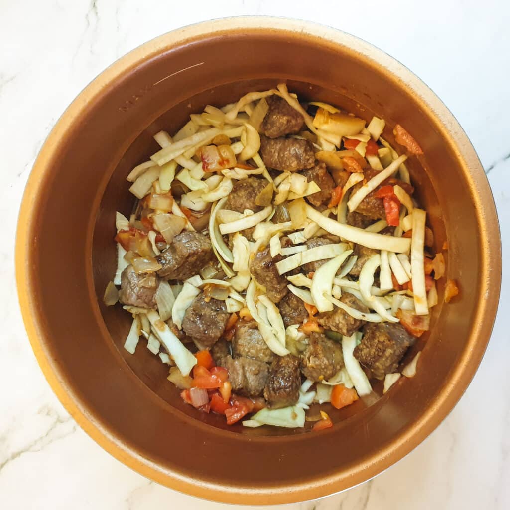 Meat and chopped vegetables stirred together in a pressure cooker.