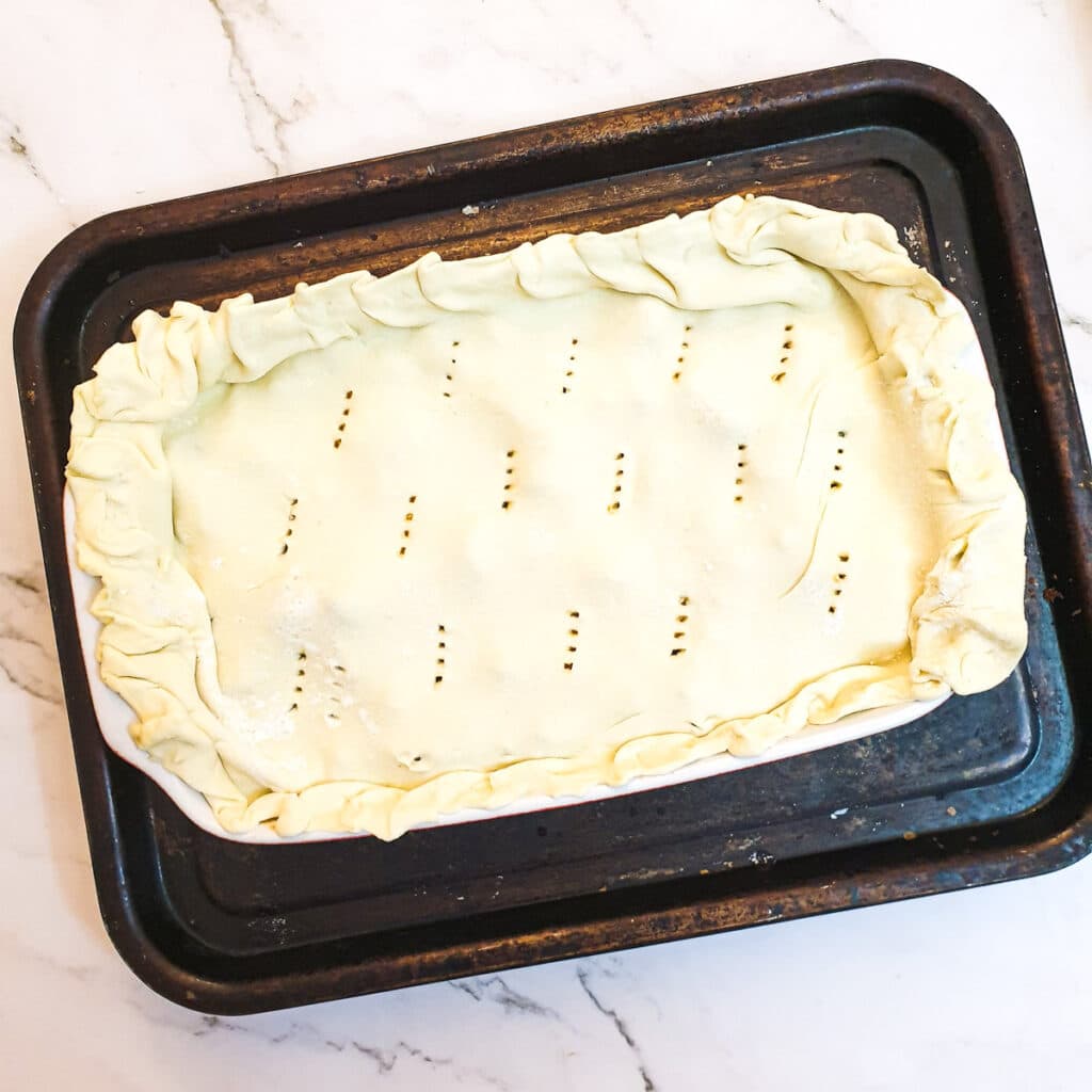 A steak and kidney pie covered with puff pastry ready to go into the oven.