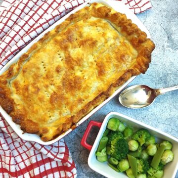 A homemade steak and kidney pie covered with golden crispy puff pastry alongside a dish of brussels sprouts.