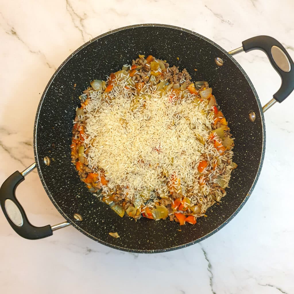 Uncooked rice being added to the pan.