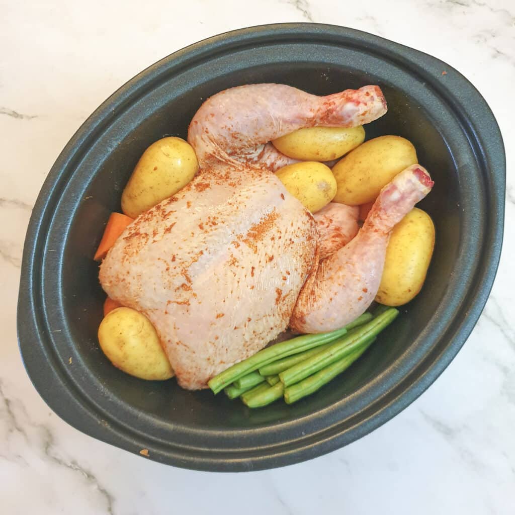 An uncooked chicken on a bed of vegetables in a slow-cooker.