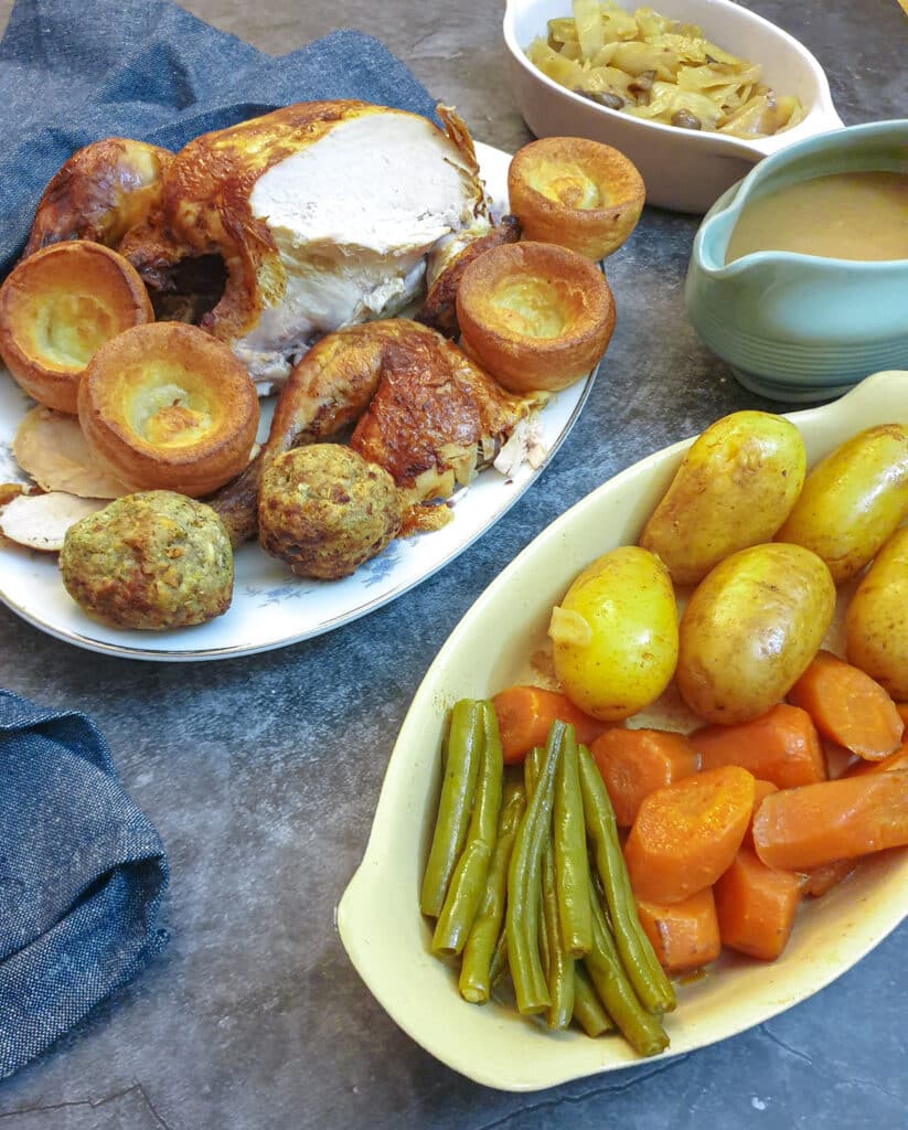 A roast chicken on a plate alongside a dish of vegetables.