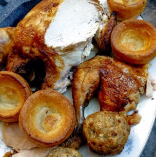 A partly carved slow-cooker roast chicken on a plate with Yorkshire puddings and stuffing balls.