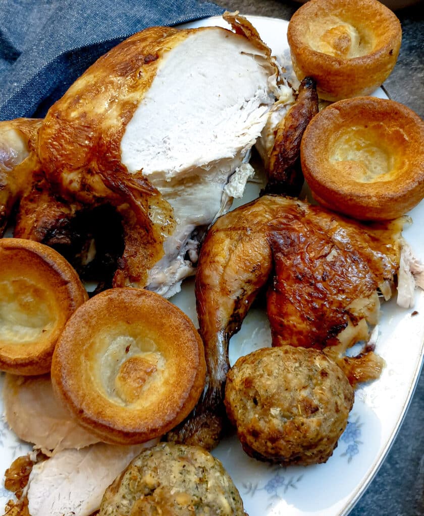 A partly carved slow-cooker roast chicken on a plate with Yorkshire puddings and stuffing balls.