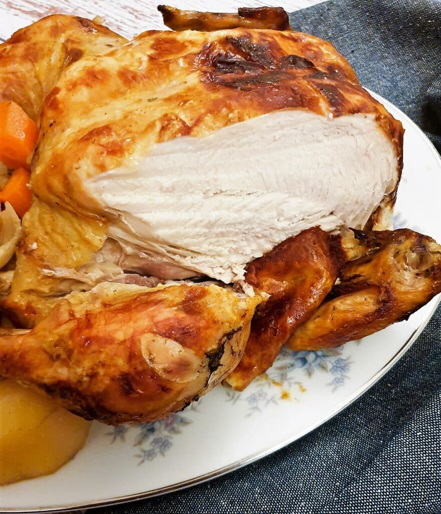 Close up of a slow-cooker roast chicken with a slice carved out of the breast.
