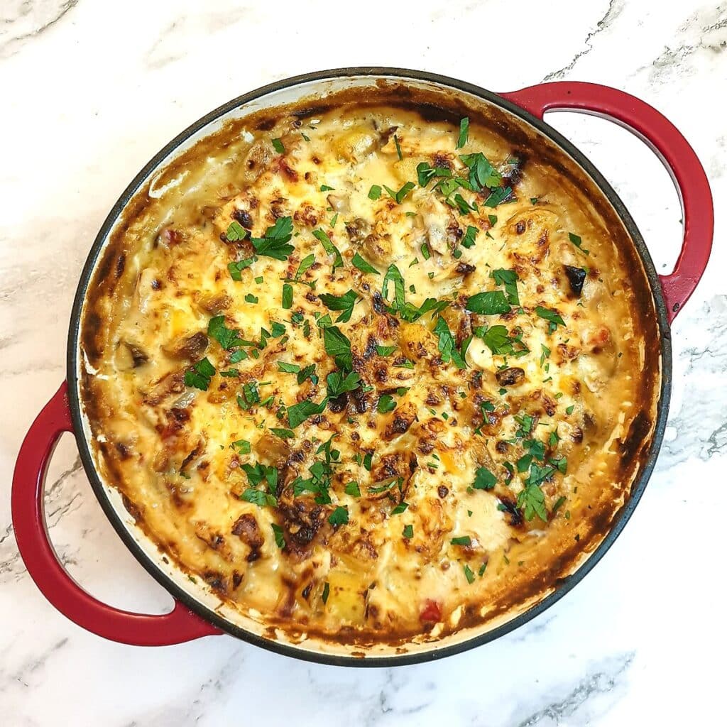 A chicken and potato bake garnished with chopped parsley after being browned in the oven.