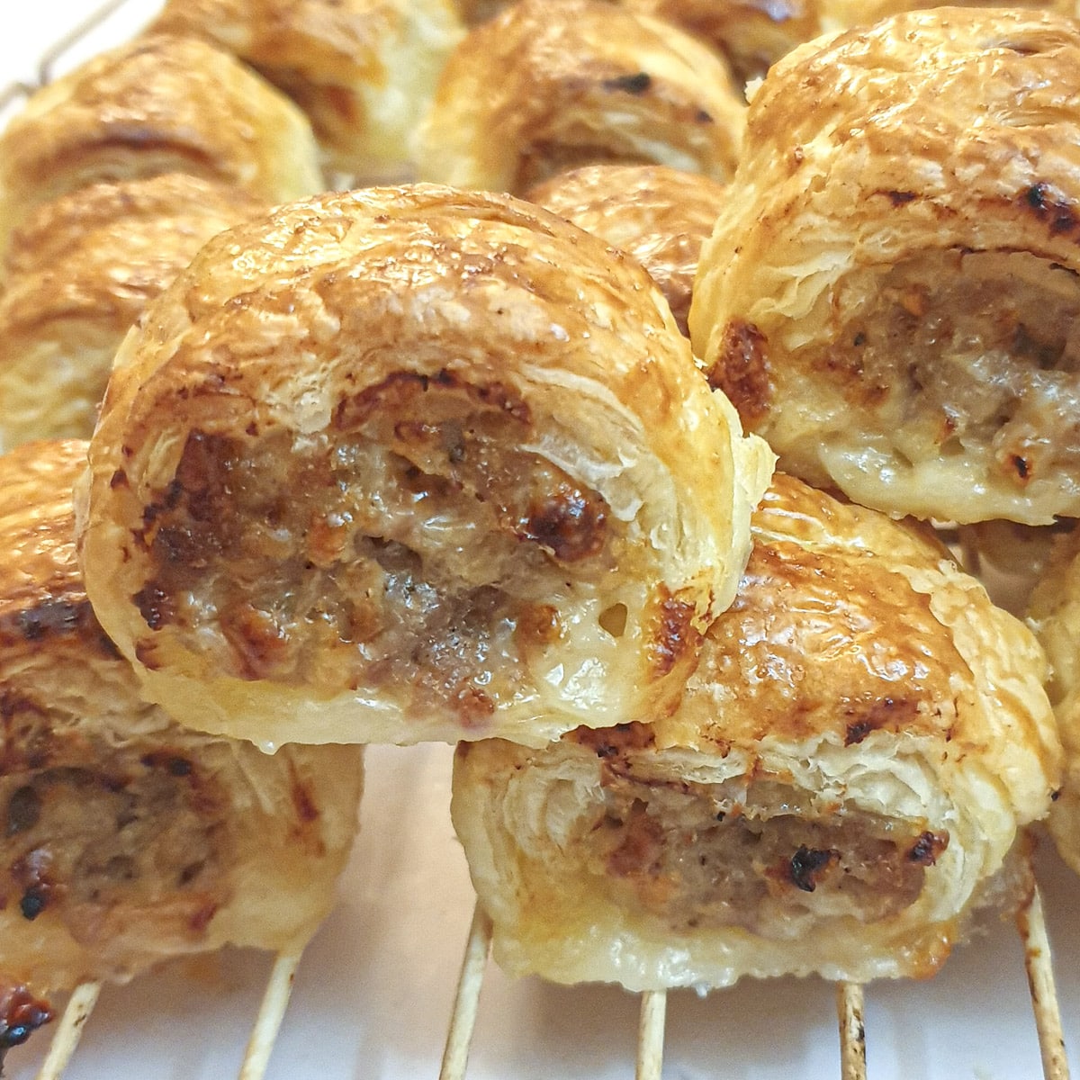 A pile of cheese and onion pork sausage rolls cooling on a rack.