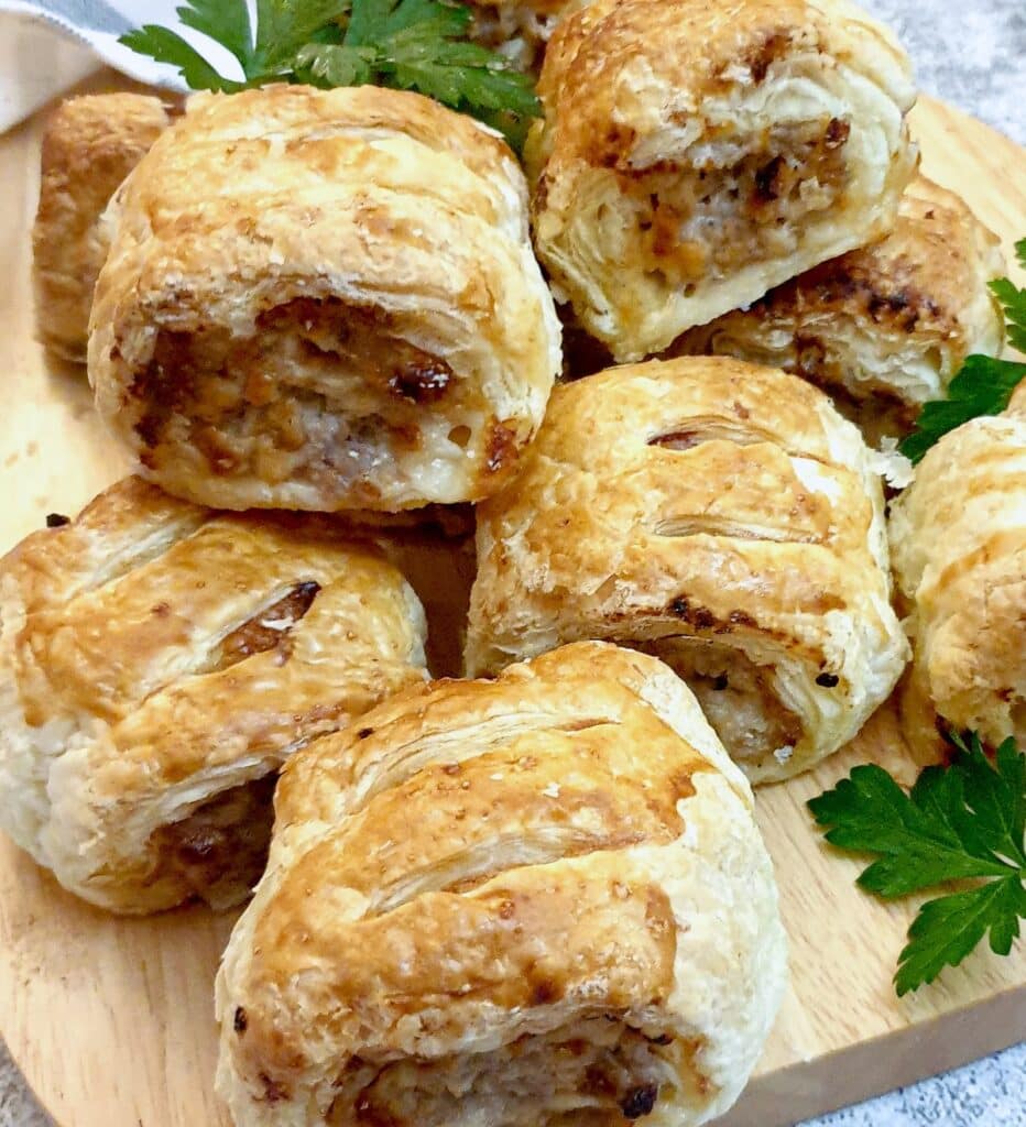 A pile of sausage rolls on a wooden board.