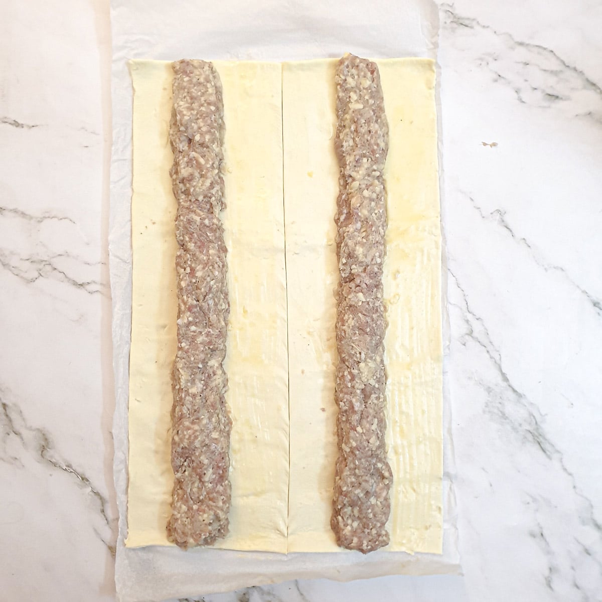 Two lengths of pork sausage meat stuffing on a sheet of puff pastry.