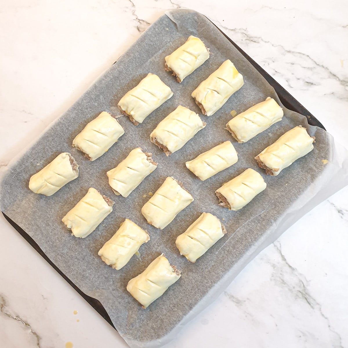 Unbaked sausage rolls on a baking tray.