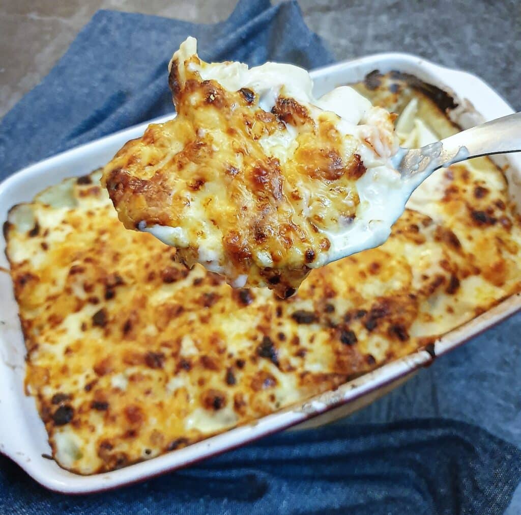 A spoonful of seafood stuffed pasta shells being lifted from the baking dish.