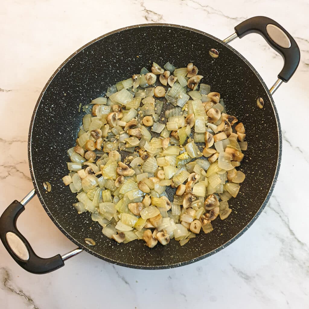 Onions and mushrooms softening in a frying pan.