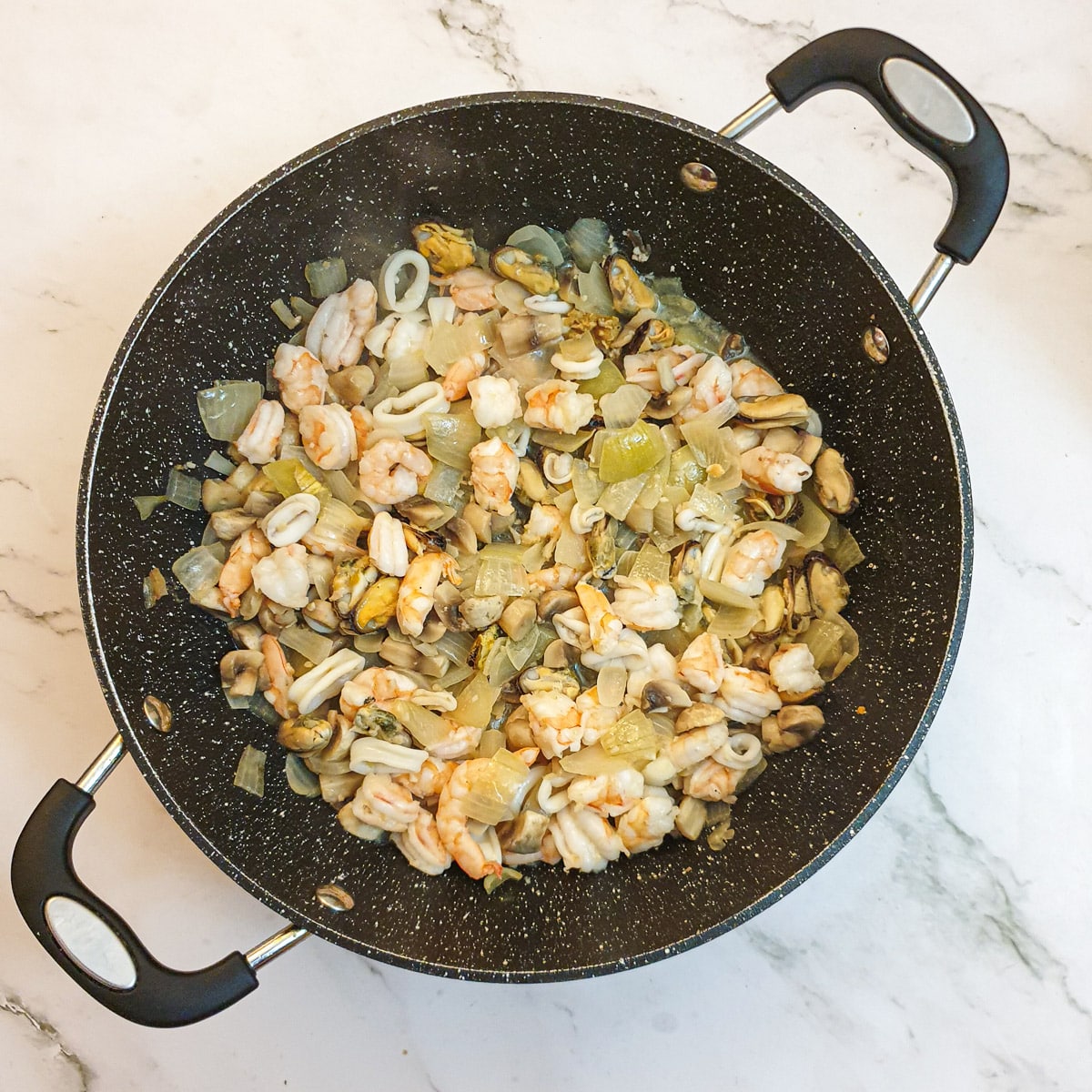 Onions and mushrooms in a frying pan with prawns and mixed seafood.