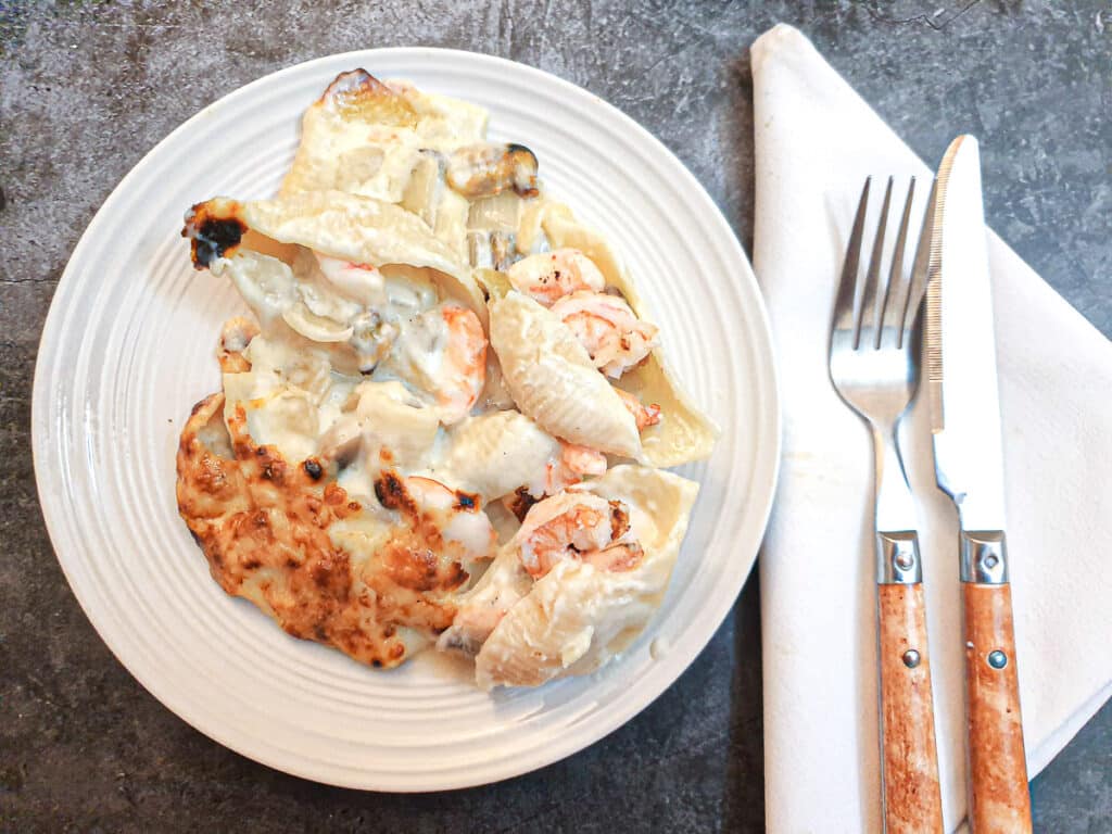 Seafood stuffed pasta shells on a white plate alongside a knife and fork.