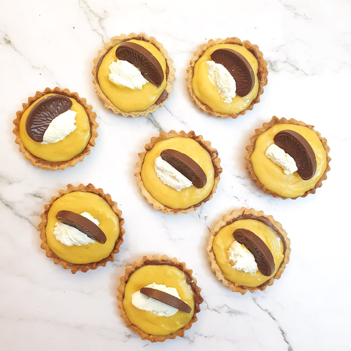 8 chocolate orange tarts decorated with whipped cream and a slice of chocolate orange.