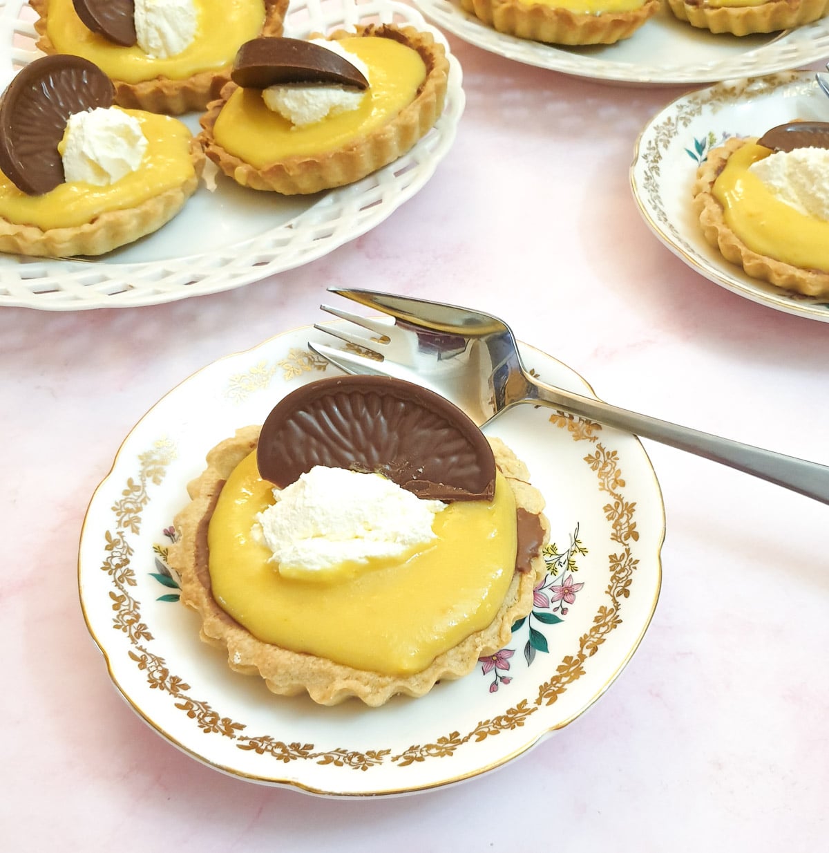 Chocolate orange tarts on plates on a pink table top.