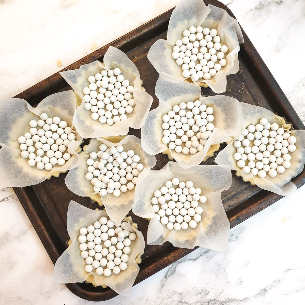 8 flan cases on a baking sheet ready to go in the oven.