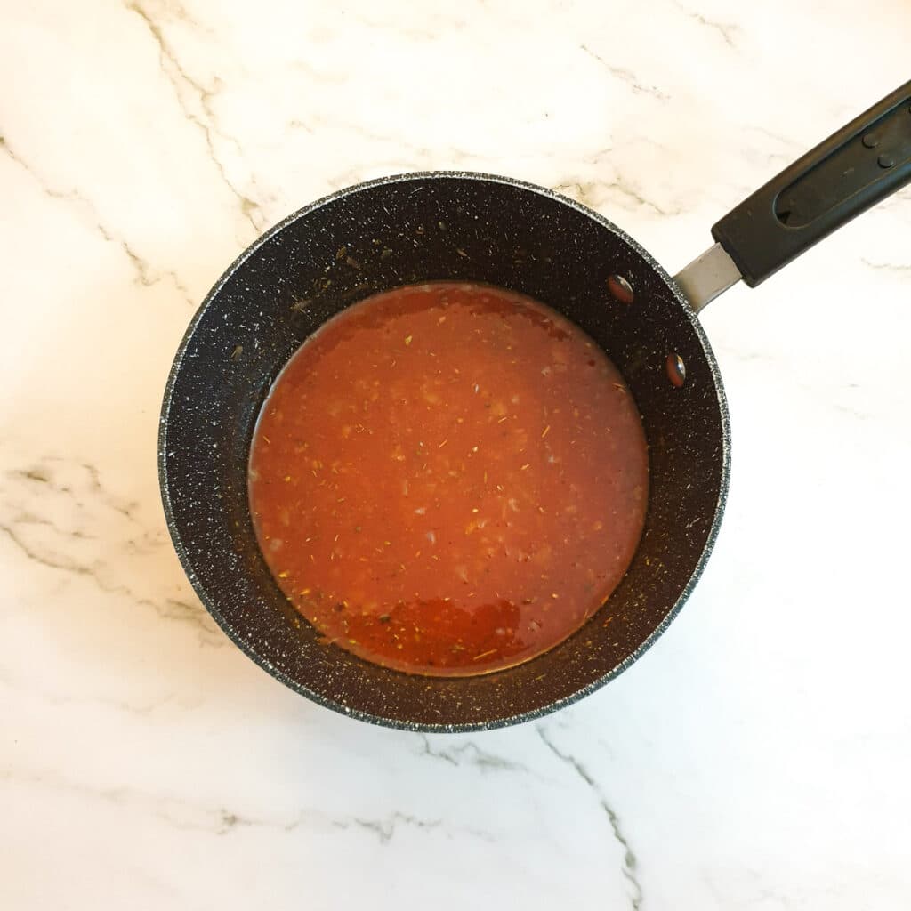 Tomato passata in a pan with onions and seasoning.