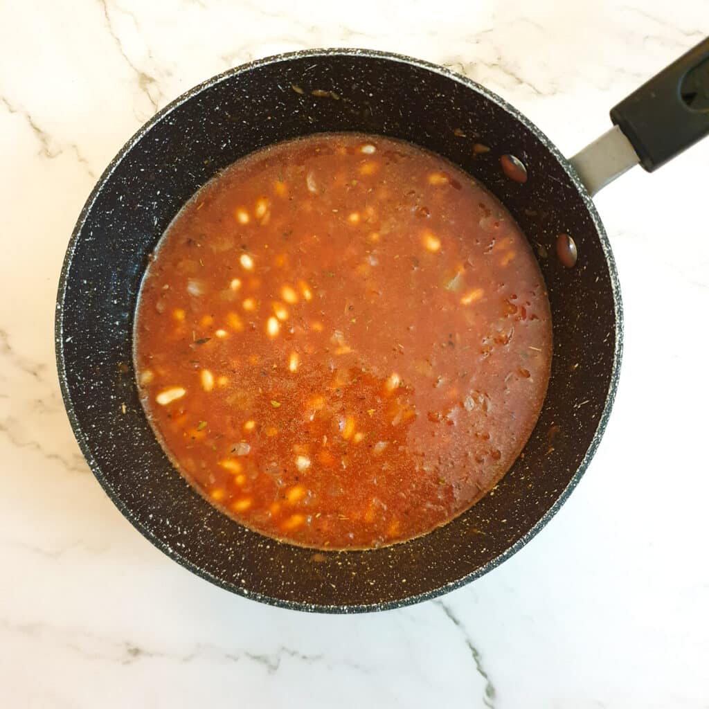 Haricot beans added to a pan of passata before being cooked.