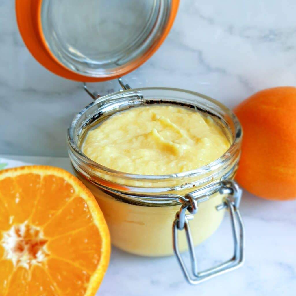 An open jar of orange curd next to half an orange.
