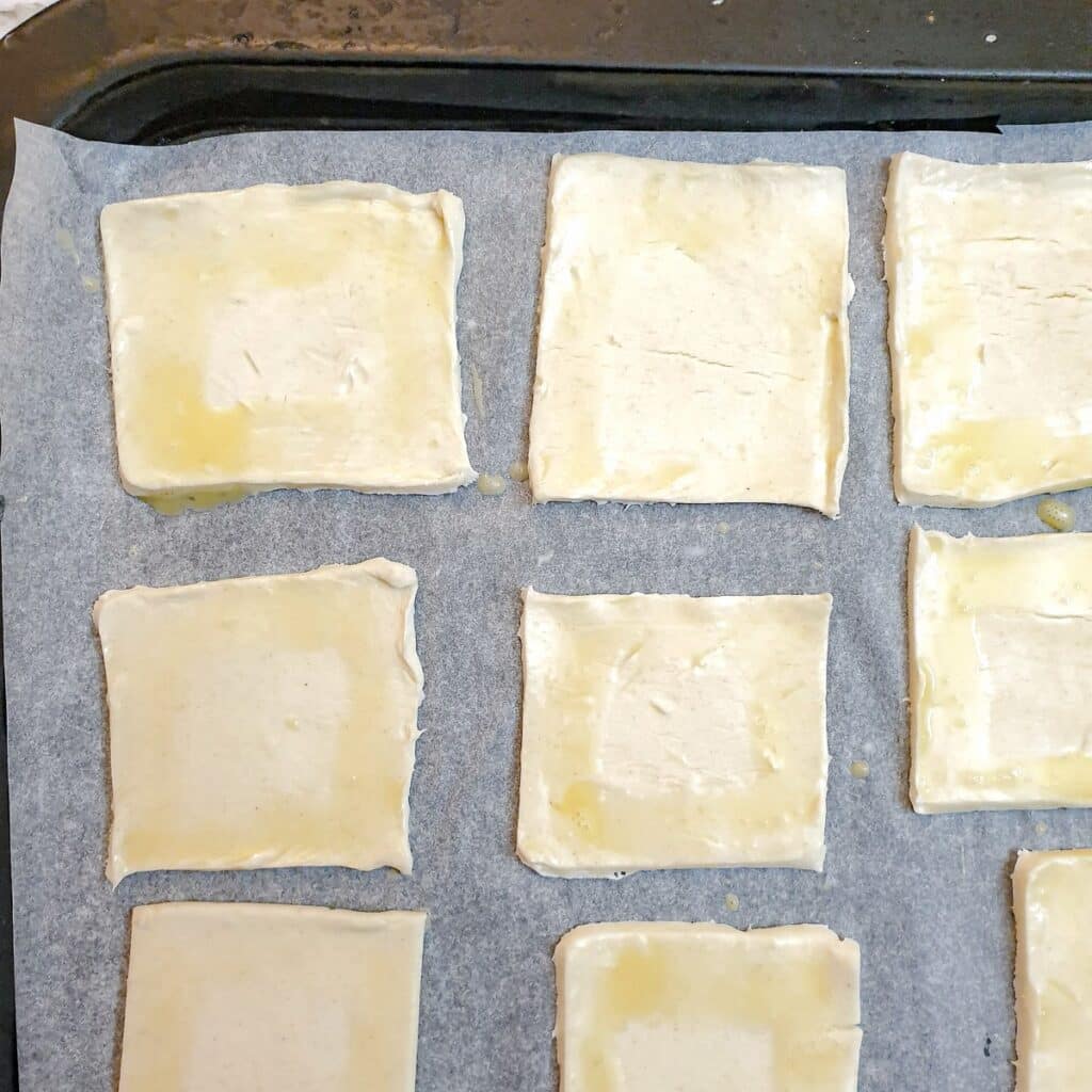 Close up of puff pastry squares brushed with egg-wash.
