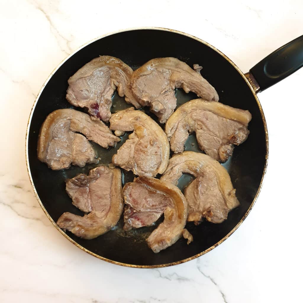 Pieces of lamb browning in a frying pan.