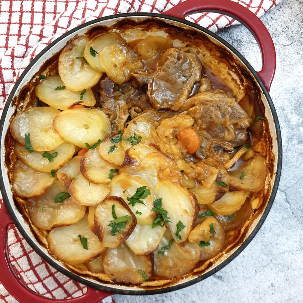 A casserole dish with lamb hotpot covered with browned sliced potatoes.