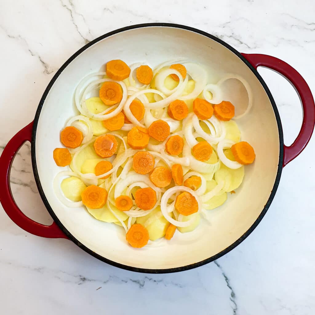 Sliced potatoes, carrots and onions on the base of a casserole dish.