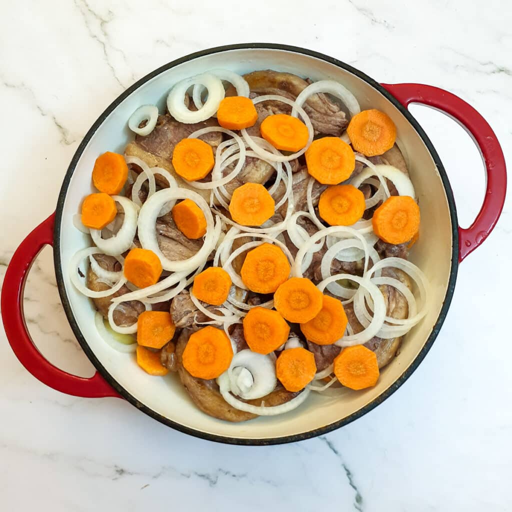 Sliced potatoes, carrots, onions and lamb in a casserole dish.