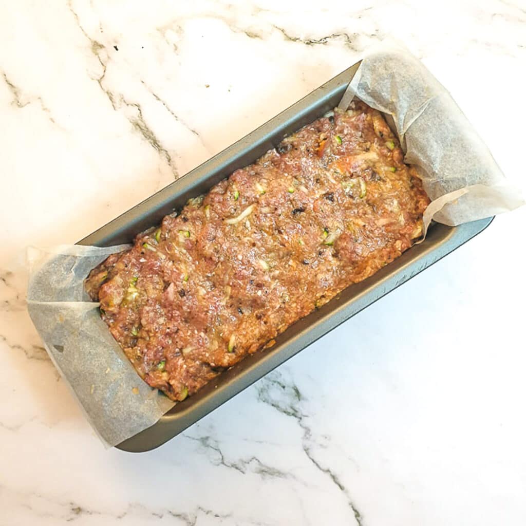 A raw meatloaf with hidden vegetables in a baking dish lined with baking parchment.
