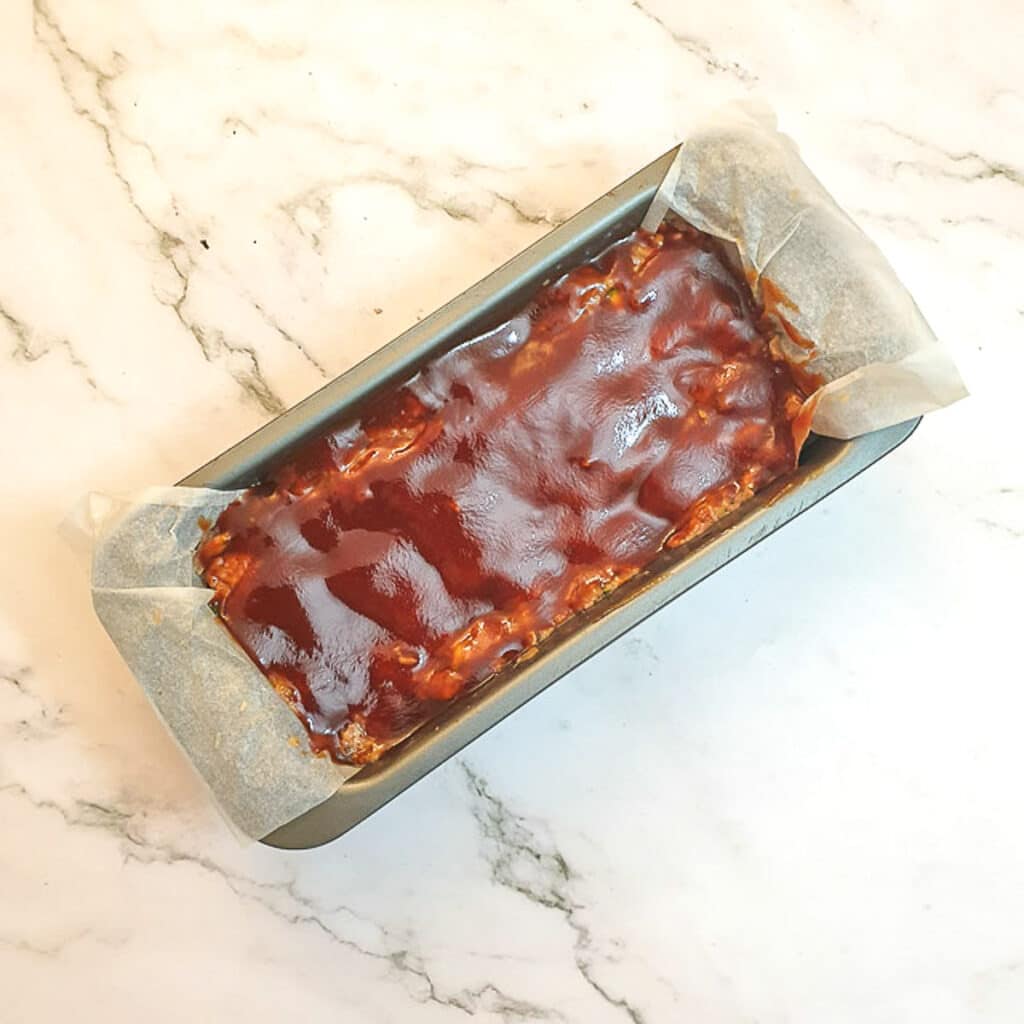 A meatloaf covered with glaze before being baked.