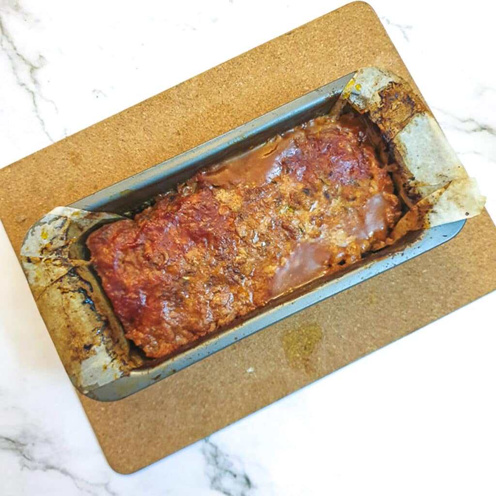 A meatloaf removed from the oven, cooling on a wooden plank.