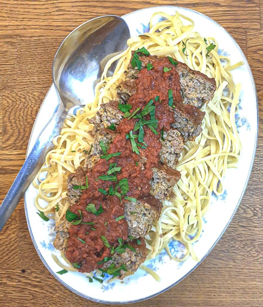 Slices of meatloaf arranged on a bed of pasta and covered with marinara sauce, on a serving platter.